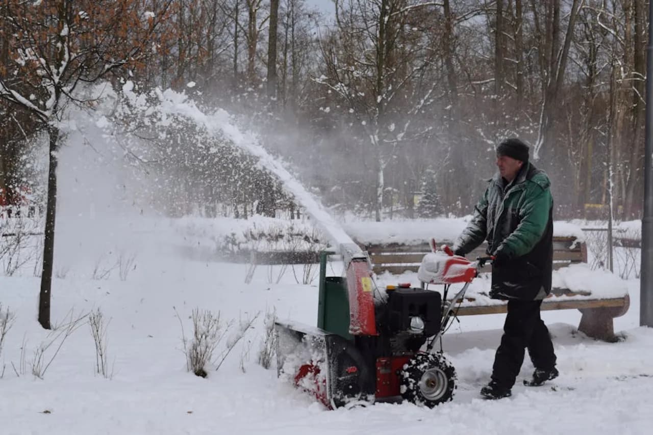 Two-stage snow blower clearing a Canadian residential driveway — gas-powered snow removal in deep winter.